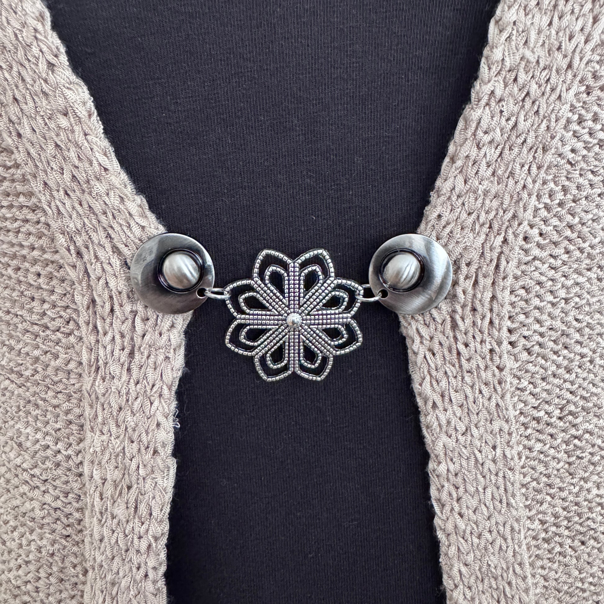 Handgemaakte zilverkleurige vestsluiting Ijsbloem van Fashionclip met opengewerkt bloemmotief op een beige vest.