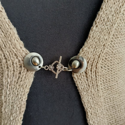 Een elegante zilverkleurige vestclip met een opengewerkte ruitvorm, bevestigd aan twee ronde magneten. De clip sluit het vest subtiel en geeft uw outfit een verfijnde uitstraling.