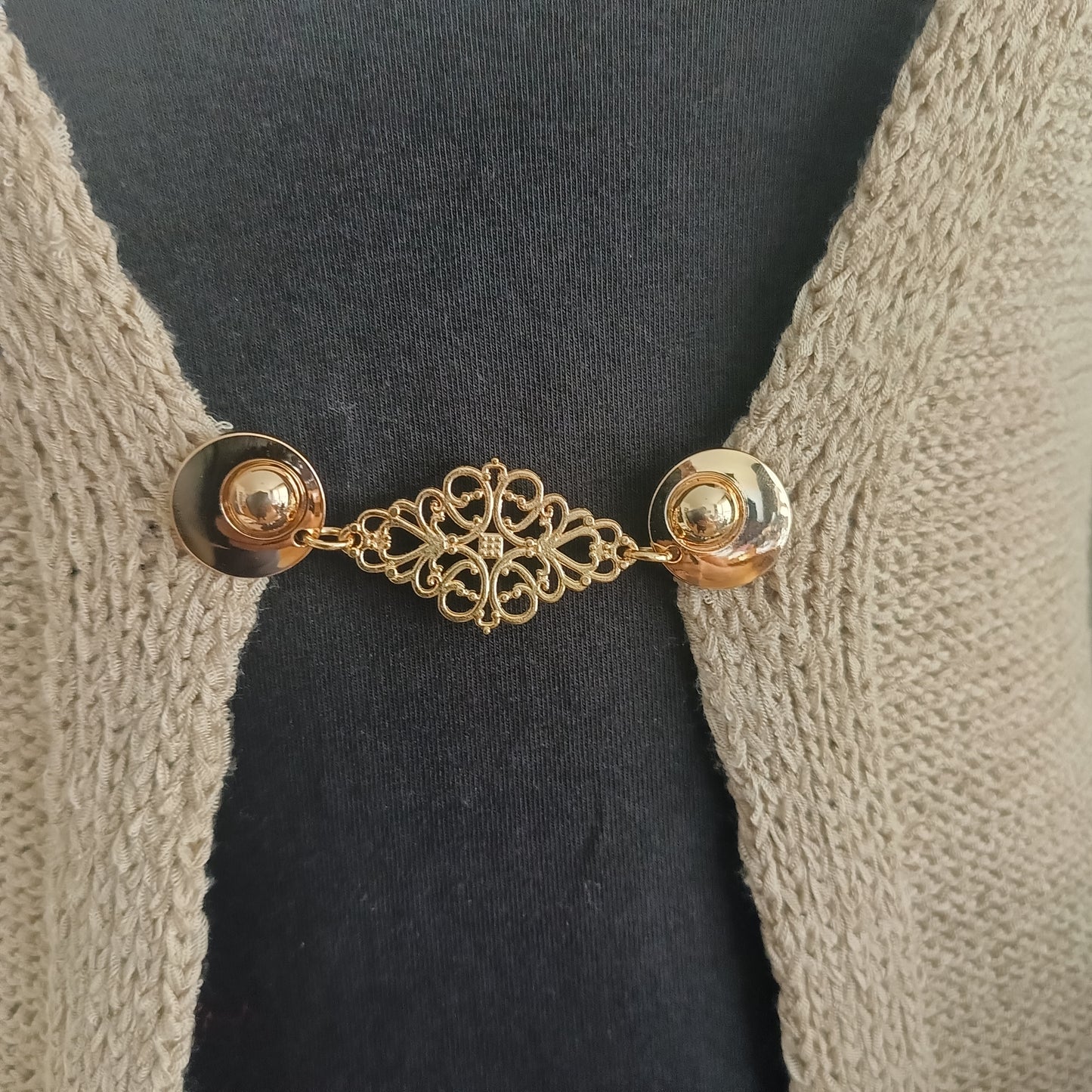 Goudkleurige Frans Brocante vestsluiting met sierlijk opengewerkt middenstuk, bevestigd op een gebreid vest voor een elegante en klassieke uitstraling.