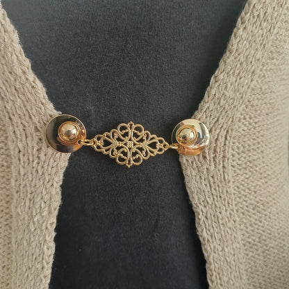 Goudkleurige Frans Brocante vestsluiting met sierlijk opengewerkt middenstuk, bevestigd op een gebreid vest voor een elegante en klassieke uitstraling.