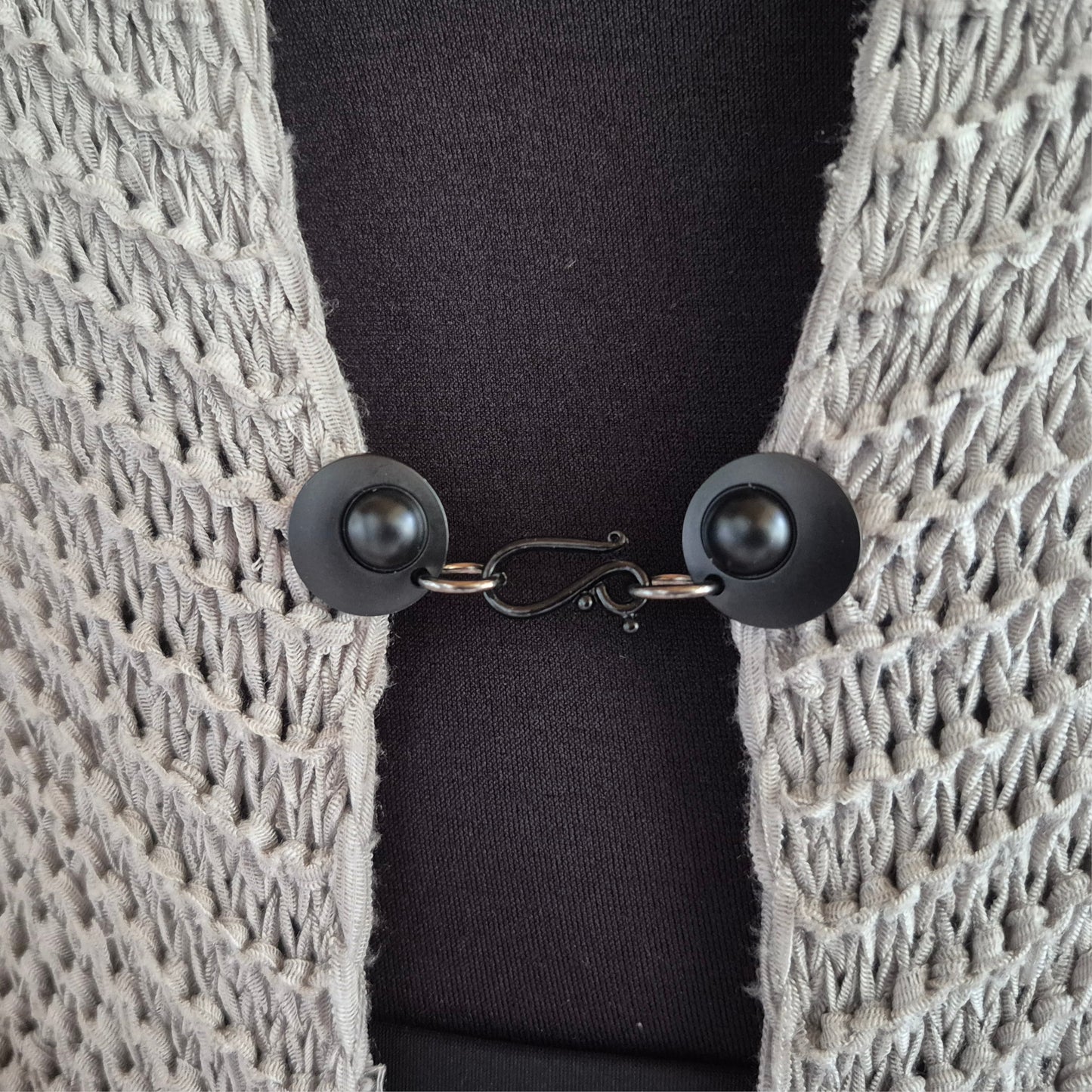 Matzwarte haak en oog vestsluiting gedragen op een licht gehaakt vest, stijlvolle Fashionclip voor het sluiten van vesten.