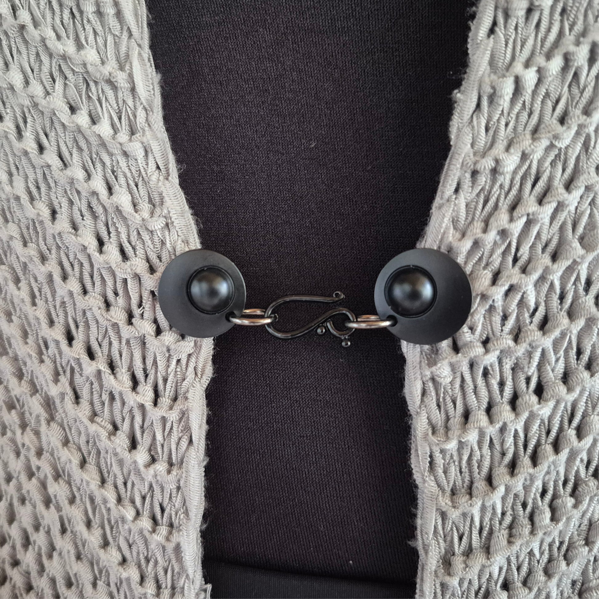 Matzwarte haak en oog vestsluiting gedragen op een licht gehaakt vest, stijlvolle Fashionclip voor het sluiten van vesten.