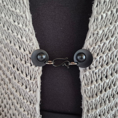 Matzwarte haak en oog vestsluiting gedragen op een licht gehaakt vest, stijlvolle Fashionclip voor het sluiten van vesten.