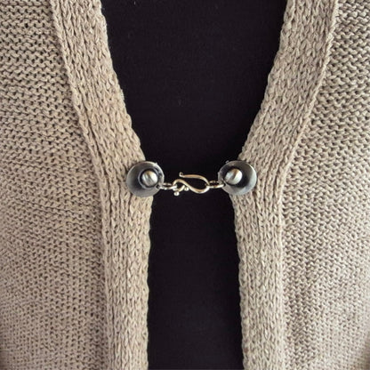Zilverkleurige haak en oog vestsluiting gedragen op een grofgebreid vest, praktische Fashionclip voor het sluiten van vesten.