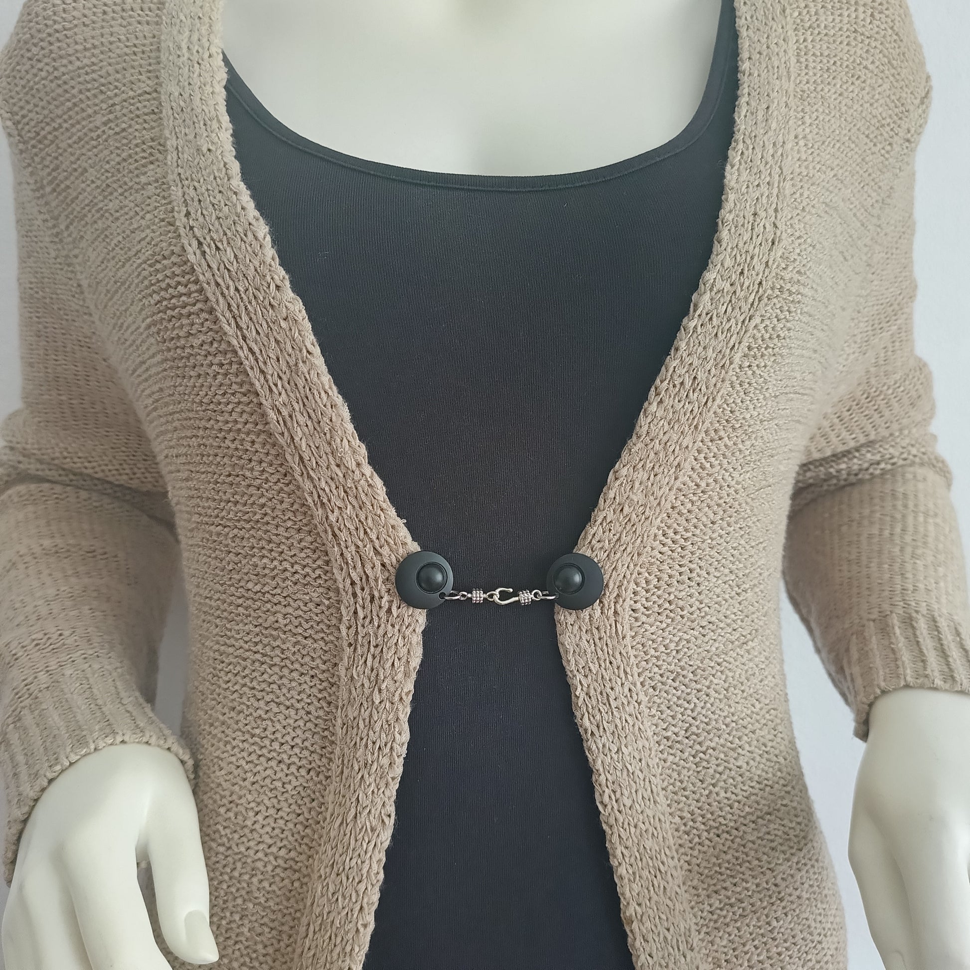 Mat zwarte vestsluiting met zilverkleurige haaksluiting, gedragen op een open gebreid vest voor een stoere uitstraling.