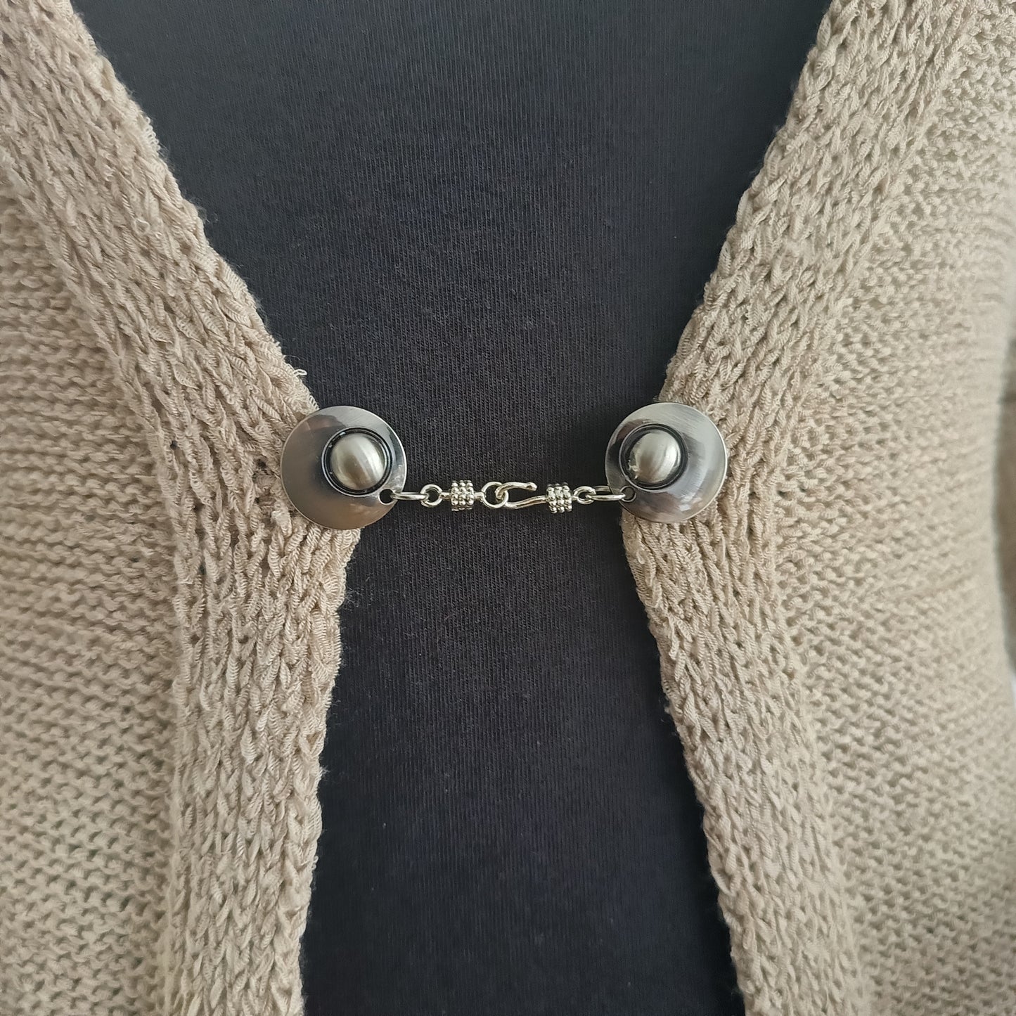 Zilverkleurige vestsluiting Kapitein Haak met haak-en-oogsluiting, stoer en tijdloos op een open gebreid vest.