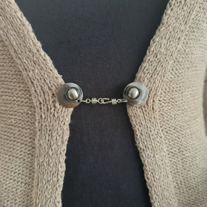 Zilverkleurige vestsluiting Kapitein Haak met haak-en-oogsluiting, stoer en tijdloos op een open gebreid vest.