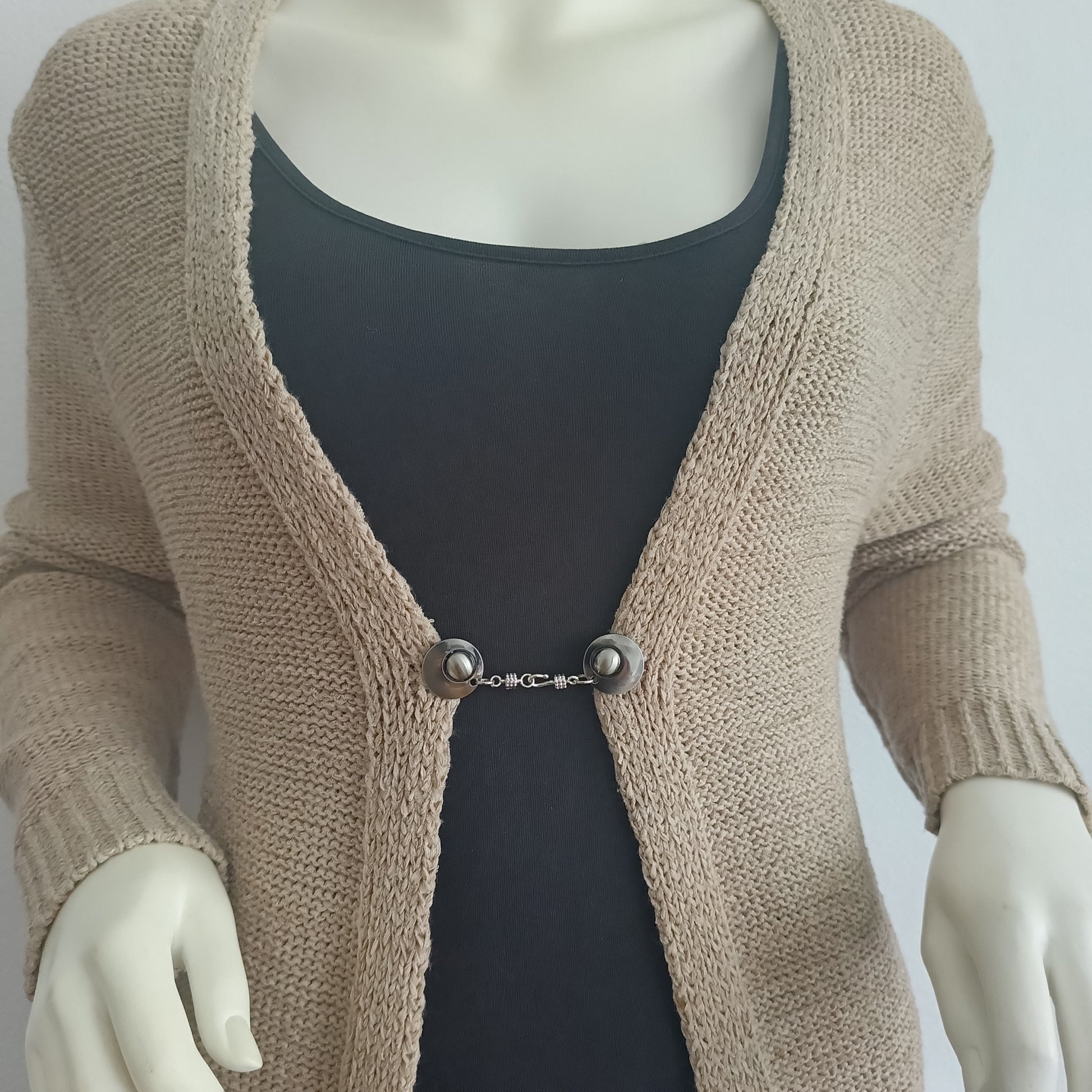 Zilverkleurige vestsluiting Kapitein Haak met haak-en-oogsluiting, gedragen op een open gebreid vest.