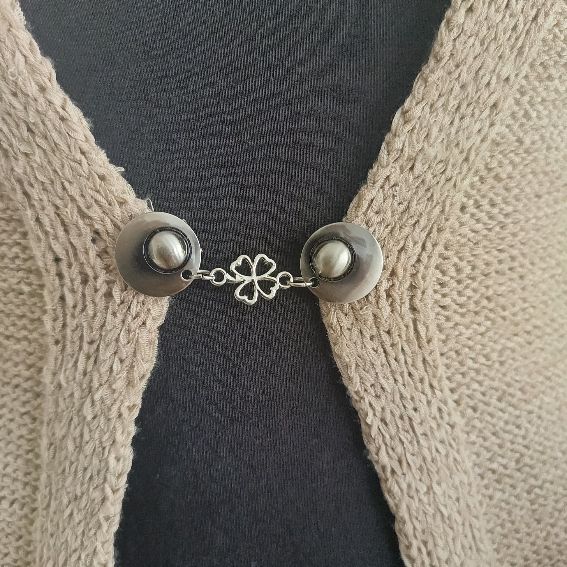 Zilverkleurige vestsluiting Klavertje Vier met subtiel klaverdetail, bevestigd aan een gebreid vest voor een elegante en vriendelijke look.