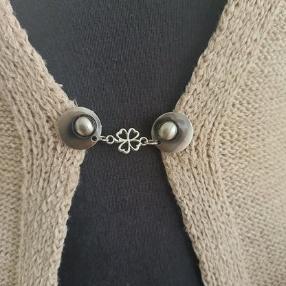 Zilverkleurige vestsluiting Klavertje Vier met subtiel klaverdetail, bevestigd aan een gebreid vest voor een elegante en vriendelijke look.