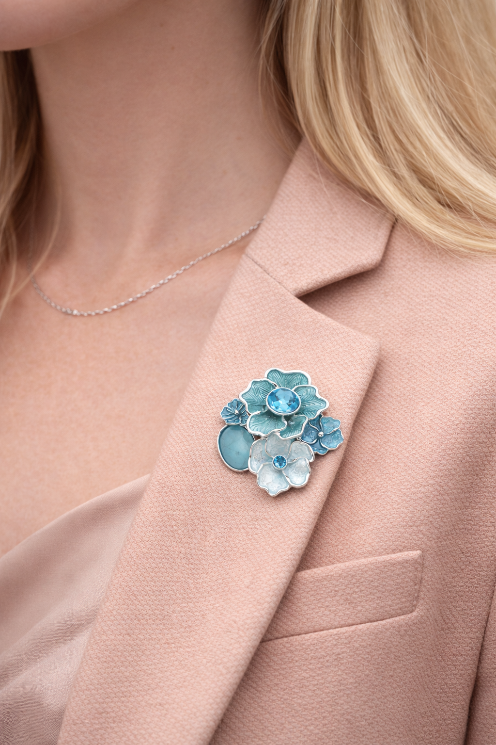 Blauwkleurige magneetbroche met bloemen en glanzende steentjes, gedragen op een zachtroze blazer