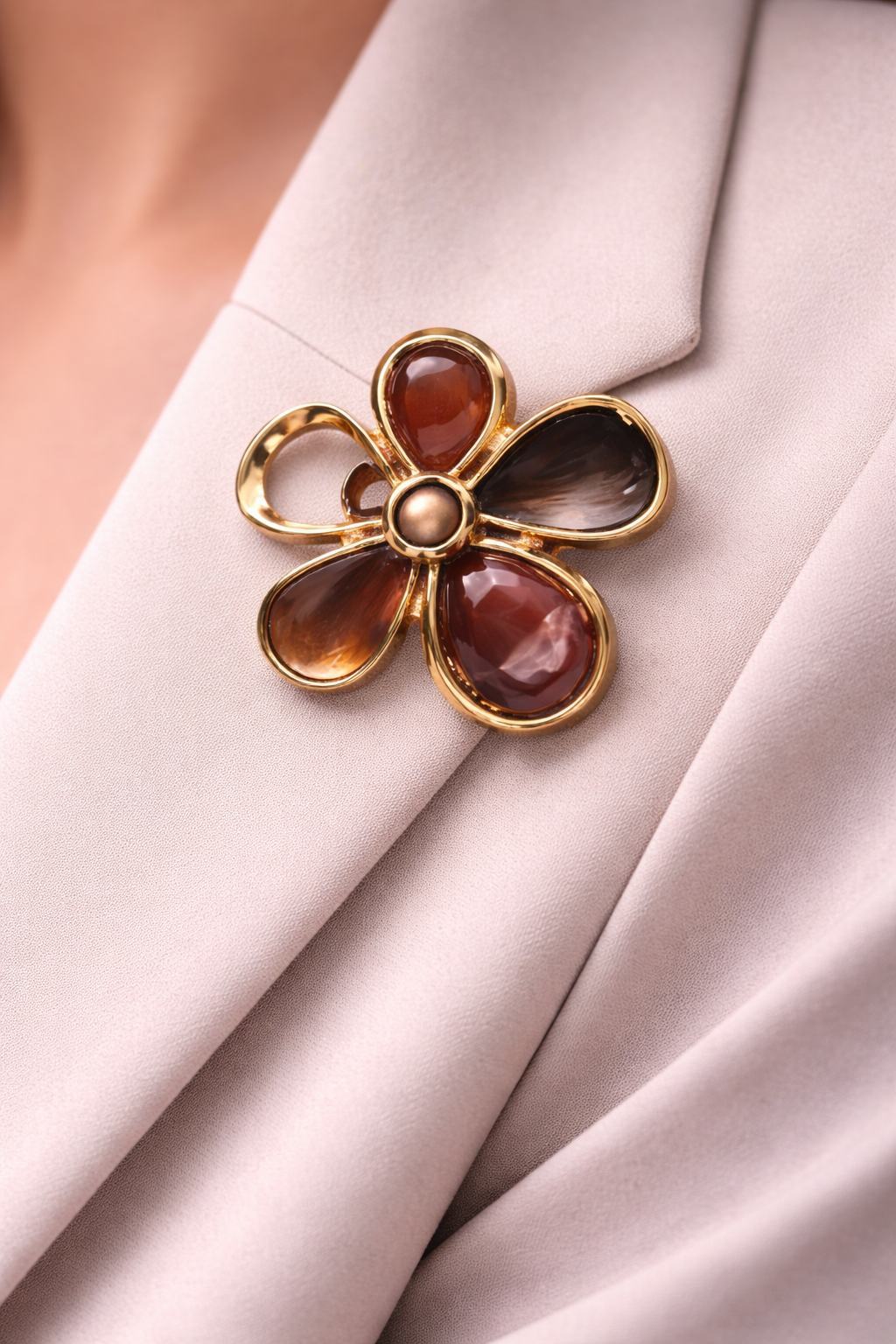 Goudkleurige magneetbroche in bloesemvorm met warme bruin- en amberkleurige stenen en een zachte glans.