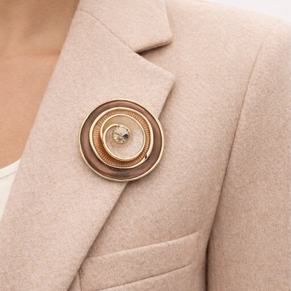 “Magneetbroche Bruine Luxe Cirkel gedragen op een colbert, warme bruin- en goudtinten met verfijnde gelaagde ringen.”