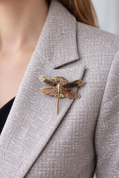 “Magneetbroche Gouden Libelle gedragen op een licht colbert, verfijnde goudkleurige vleugels met subtiele roze accenten.”