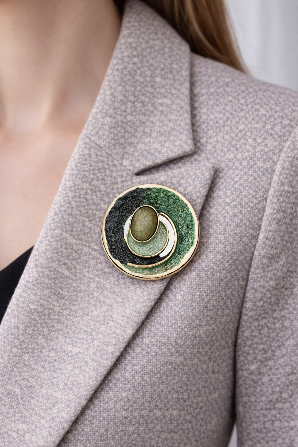 “Magneetbroche Groene Harmonie gedragen op een licht colbert, diepe groentinten met goudkleurige omlijsting.”