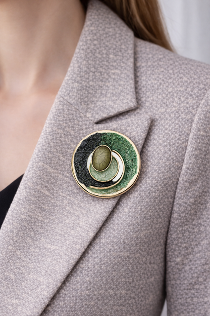 “Magneetbroche Groene Harmonie gedragen op een licht colbert, diepe groentinten met goudkleurige omlijsting.”