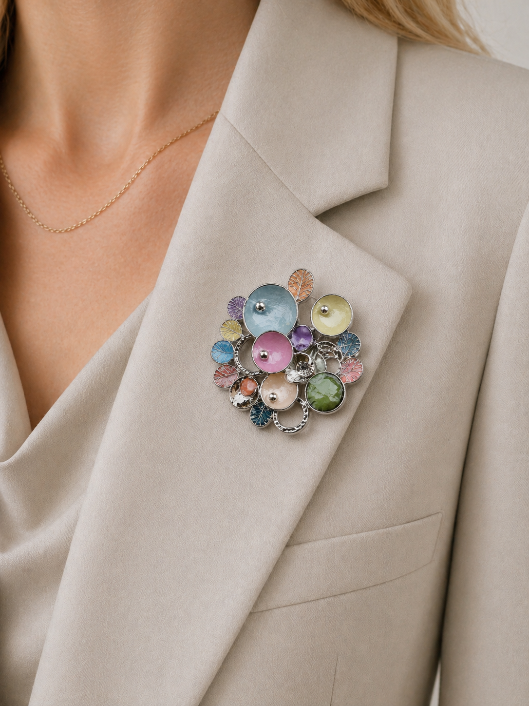 Magneetbroche met kleurrijke cirkels gedragen op een licht colbert, elegante damesbroche in zachte pastelkleuren en zilverkleurige details.