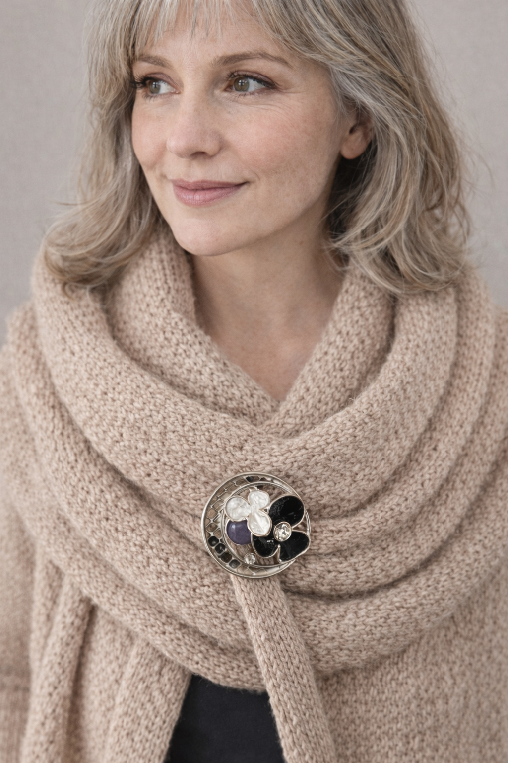 “Magneetbroche Middernacht Bloemencirkel gedragen op een beige sjaal, combinatie van zwart en zilver met elegante uitstraling.”