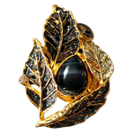 Zwart-gouden magneetbroche in bladvorm met verfijnde nervenstructuur en glanzende zwarte steen. Deze elegante broche zonder speld combineert natuurlijke vormen met een luxe uitstraling en tijdloze klasse.