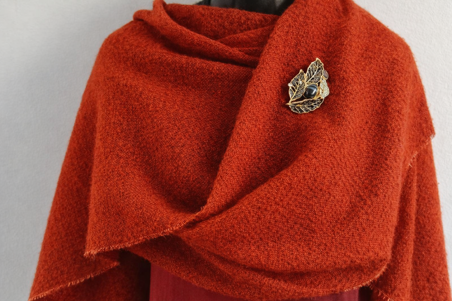 Magneetbroche Nr.01 Zwart Gouden Blad gedragen op een warme rode omslagdoek, elegante broche met bladmotief in zwart- en goudtinten.