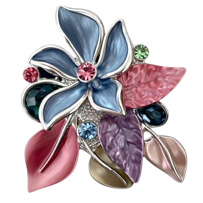 Kleurrijke magneetbroche met blauwe bloem, roze en paarse bladeren en fonkelende steentjes. Deze elegante broche zonder speld brengt kleur, speelsheid en verfijning samen in één opvallend sieraad.