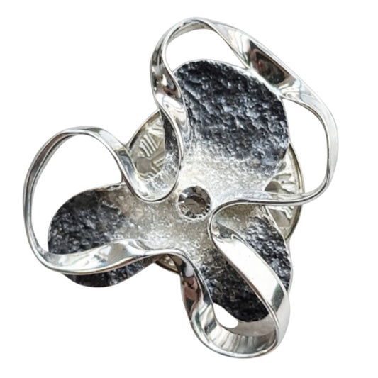 Abstracte zilverkleurige magneetbroche met sierlijke organische vormen, donkere accenten en een subtiele strasssteen in het midden. Een moderne broche zonder speld voor een stijlvolle en eigentijdse uitstraling.
