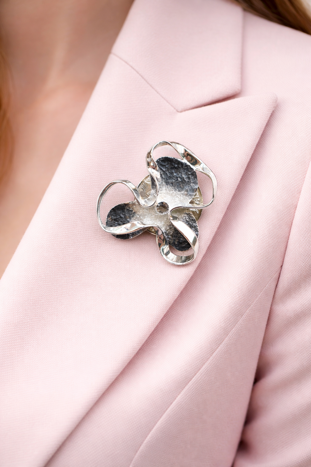 Magneetbroche Nr.30 Abstracte Rozet gedragen op een licht colbert, elegante damesbroche met organische vormen en zilverkleurige details.