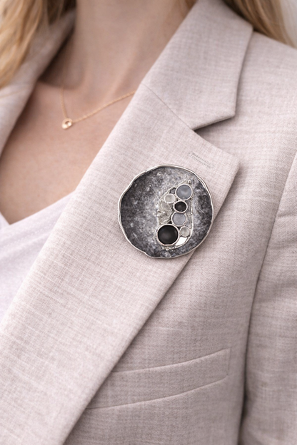 Magneetbroche Nr.42 Zwarte pracht gedragen op een licht colbert, elegante damesbroche met zwart- en grijstinten en ronde accenten.