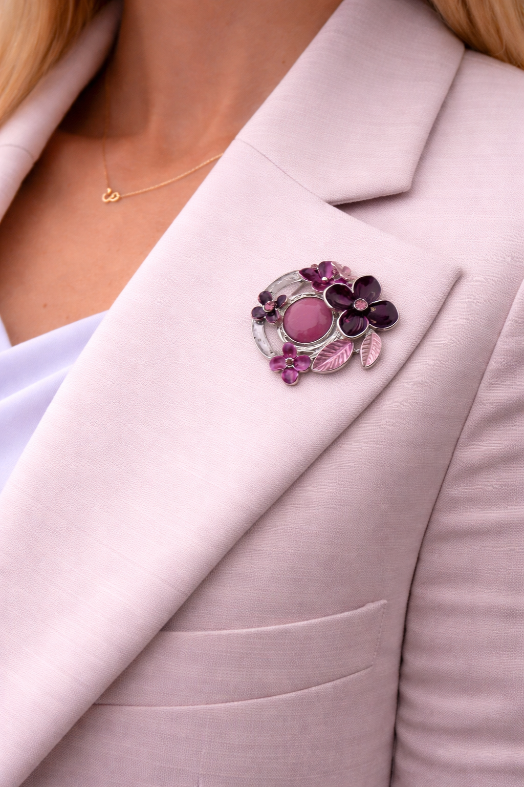 Magneetbroche paars/roze Bloemenkring gedragen op een licht colbert, bloemen in paars en roze met zilverkleurige accenten.