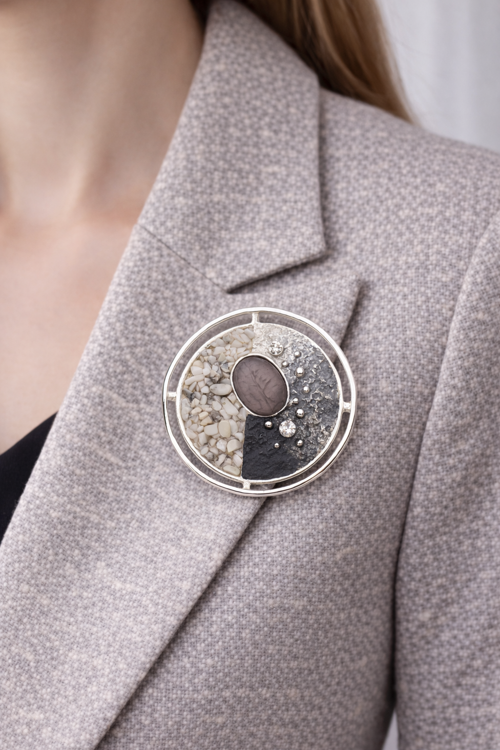 “Magneetbroche Zilveren Mozaïek Cirkel gedragen op een licht colbert, combinatie van zilver, grijs en natuursteen in ronde vorm.”