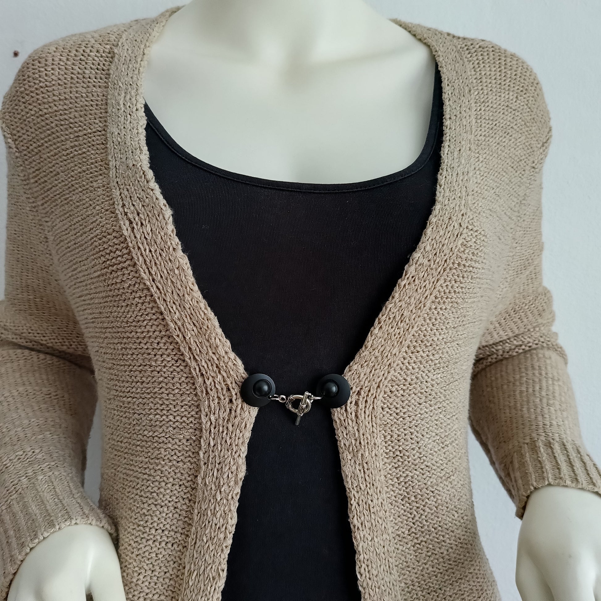 Vestclip Evenwicht in zwart met zilverkleurige details, elegant bevestigd aan een gebreid vest. De clip geeft uw outfit een rustige en stijlvolle balans.