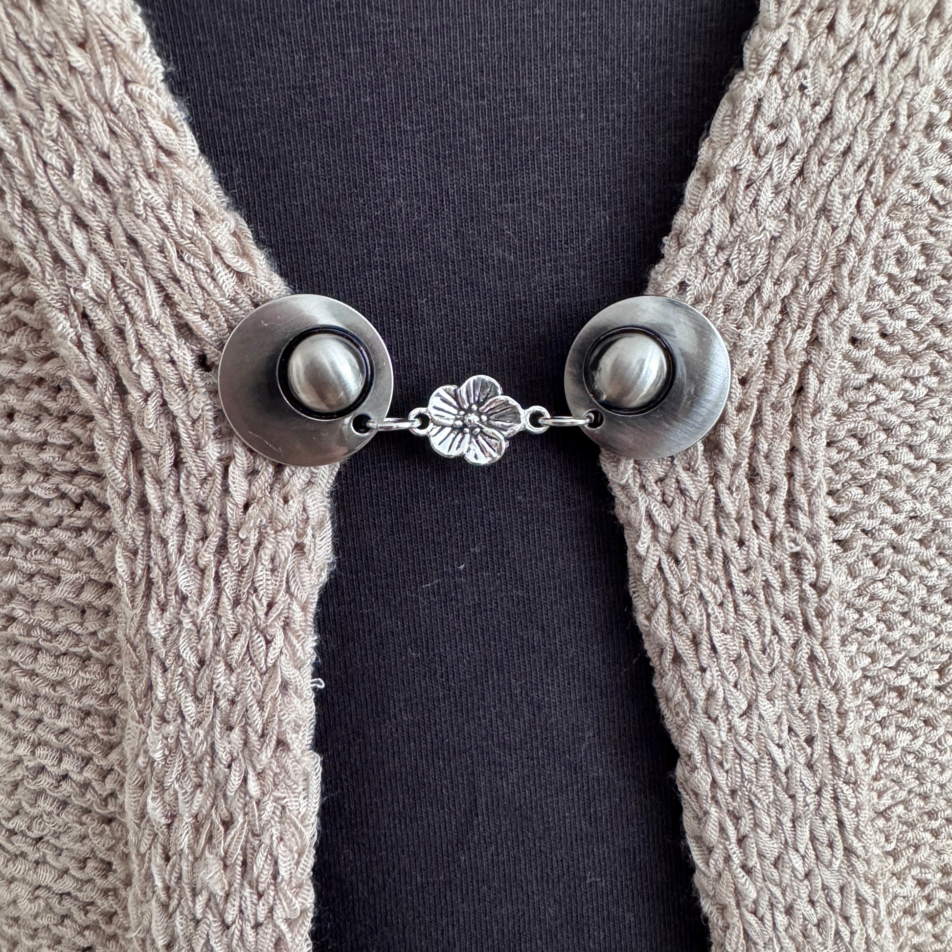 Vestsluiting Bloesem in close-up op een gebreid vest, elegante Fashionclip met zilverkleurige clips en verfijnde bloembedel.