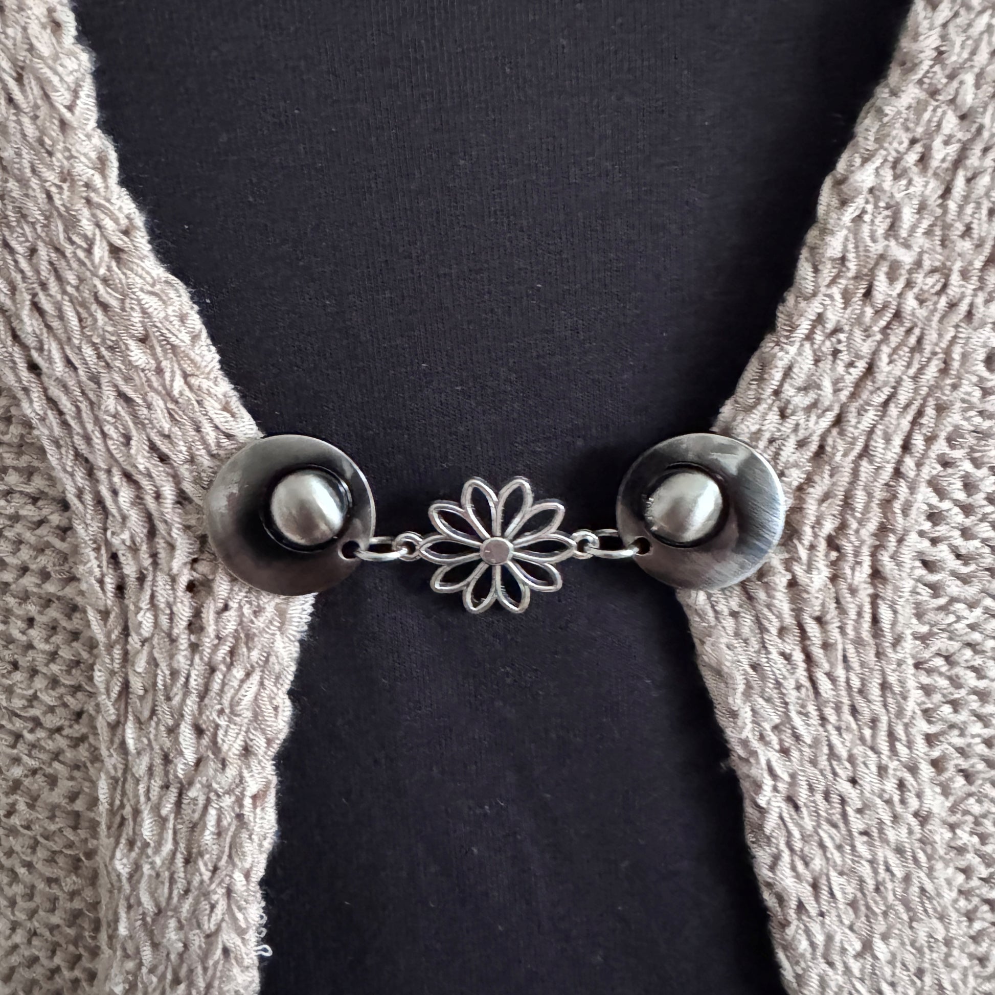 Vestsluiting Daisy zilver in close-up op een gebreid vest, elegante Fashionclip met zilverkleurige clips en open bloem tussenbedel.
