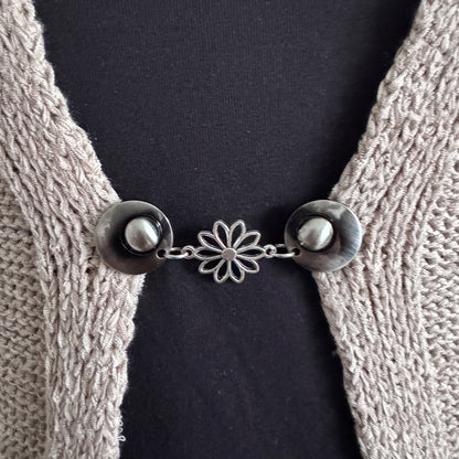 Vestsluiting Daisy zilver in close-up op een gebreid vest, elegante Fashionclip met zilverkleurige clips en open bloem tussenbedel.