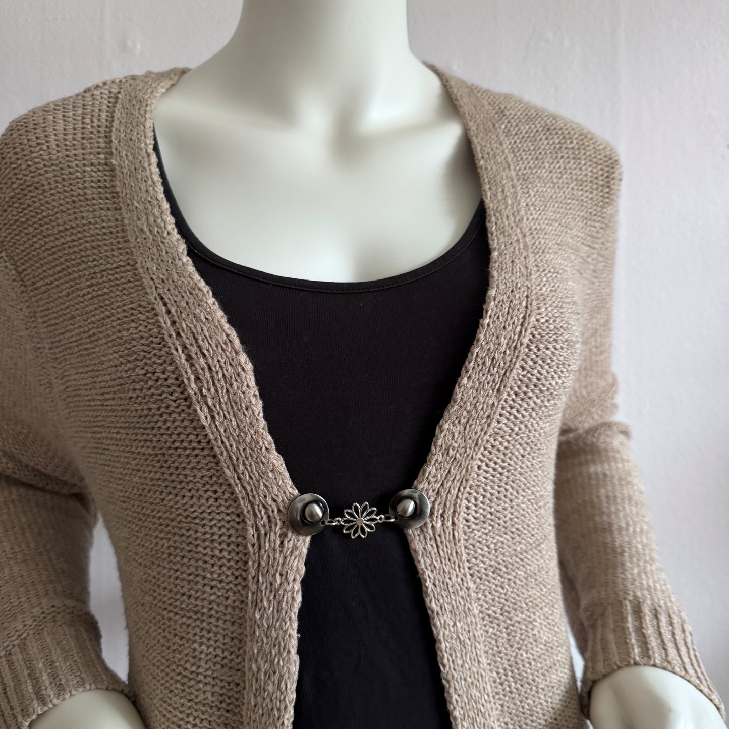 Vestsluiting Daisy zilver gedragen op een beige gebreid vest, elegante Fashionclip met zilverkleurige clips en bloemvormige tussenbedel.