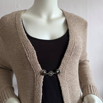 Vestsluiting Daisy zilver gedragen op een beige gebreid vest, elegante Fashionclip met zilverkleurige clips en bloemvormige tussenbedel.