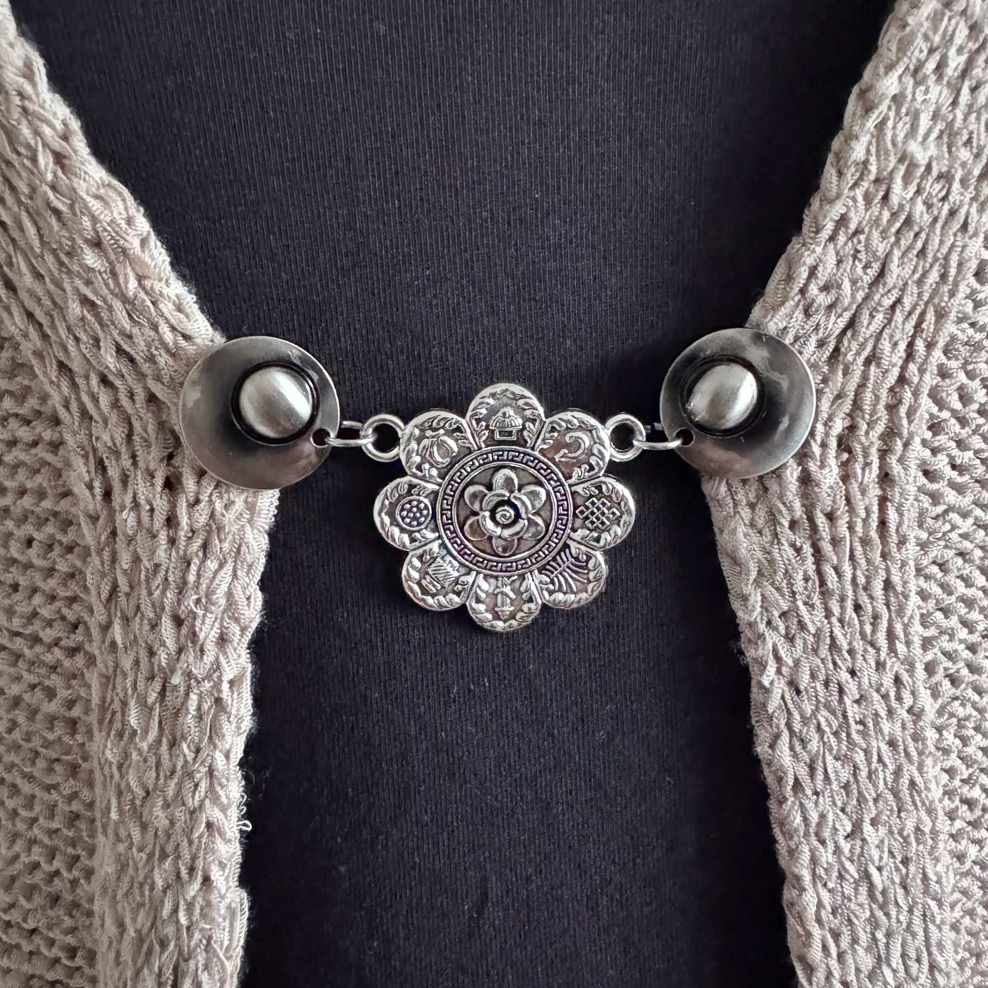 Vestsluiting De Acht Zegeningen in close-up op een gebreid vest, elegante Fashionclip met zilverkleurige clips en sierlijke mandala tussenbedel.