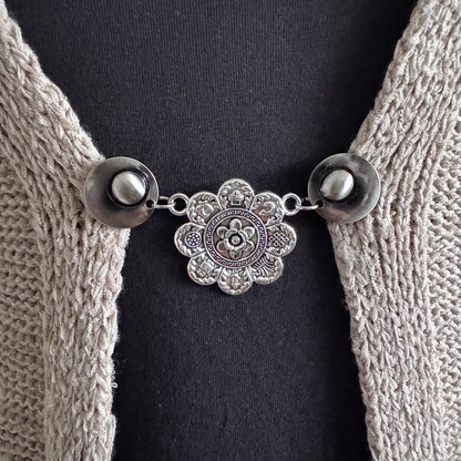 Vestsluiting De Acht Zegeningen in close-up op een gebreid vest, elegante Fashionclip met zilverkleurige clips en sierlijke mandala tussenbedel.