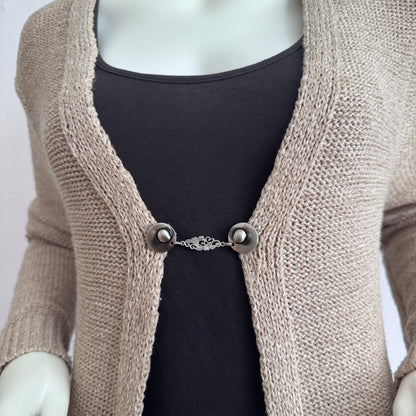Vestsluiting De Barok gedragen op een beige gebreid vest, elegante Fashionclip met zilverkleurige clips en sierlijke barok tussenbedel.