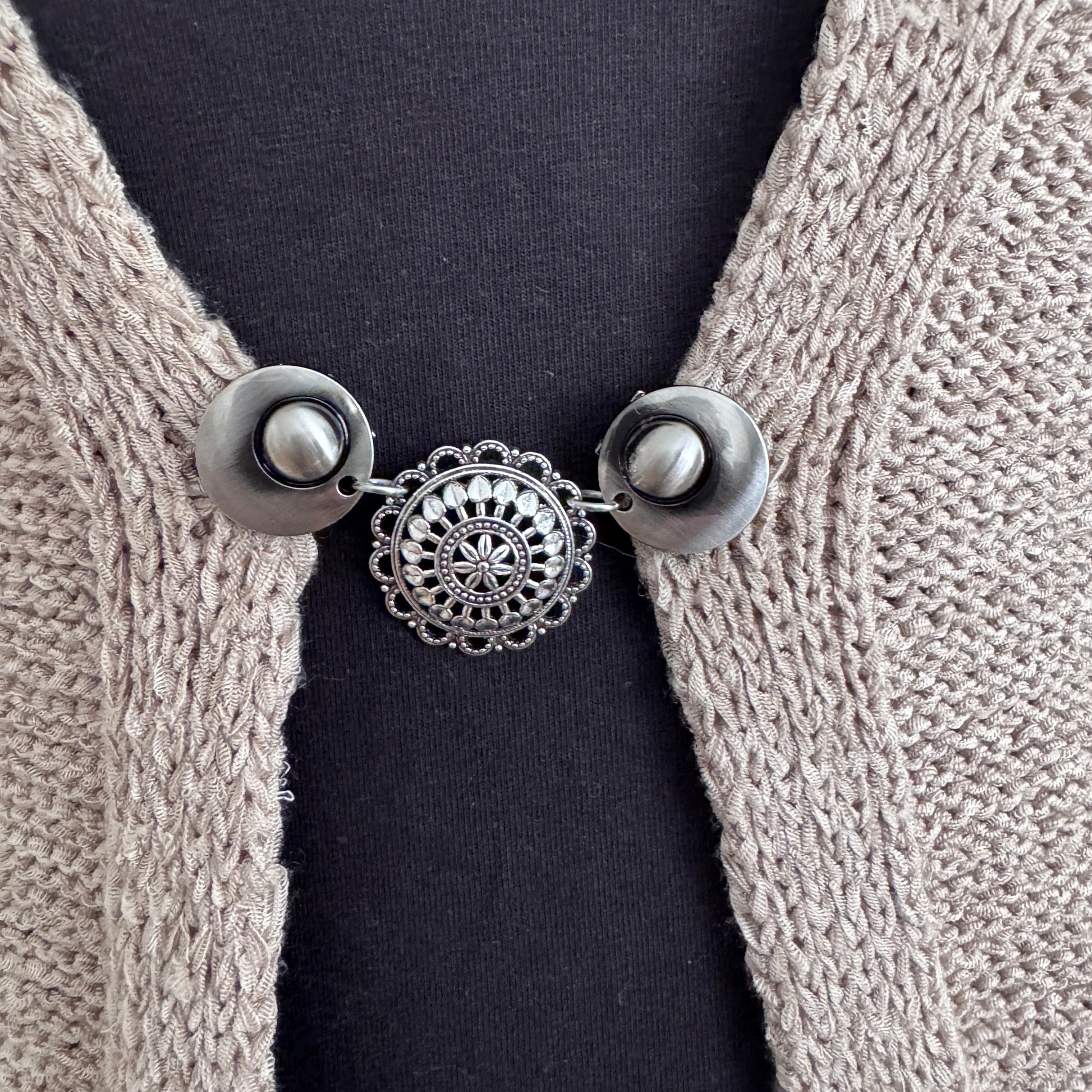 Vestsluiting De Barones in close-up op een gebreid vest, elegante Fashionclip met zilverkleurige clips en sierlijke ronde tussenbedel.