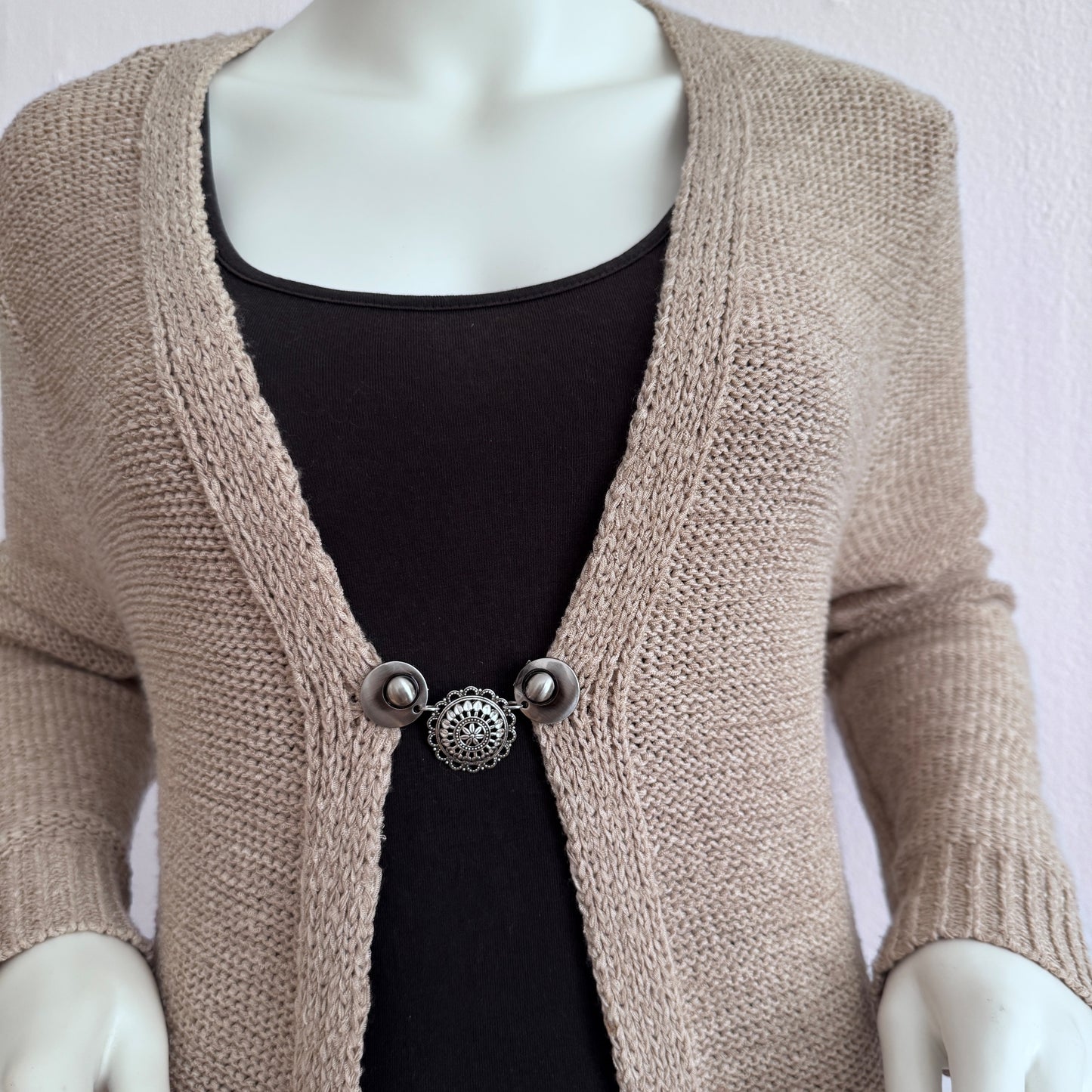 Vestsluiting De Barones gedragen op een beige gebreid vest, elegante Fashionclip met zilverkleurige clips en sierlijke ronde tussenbedel.