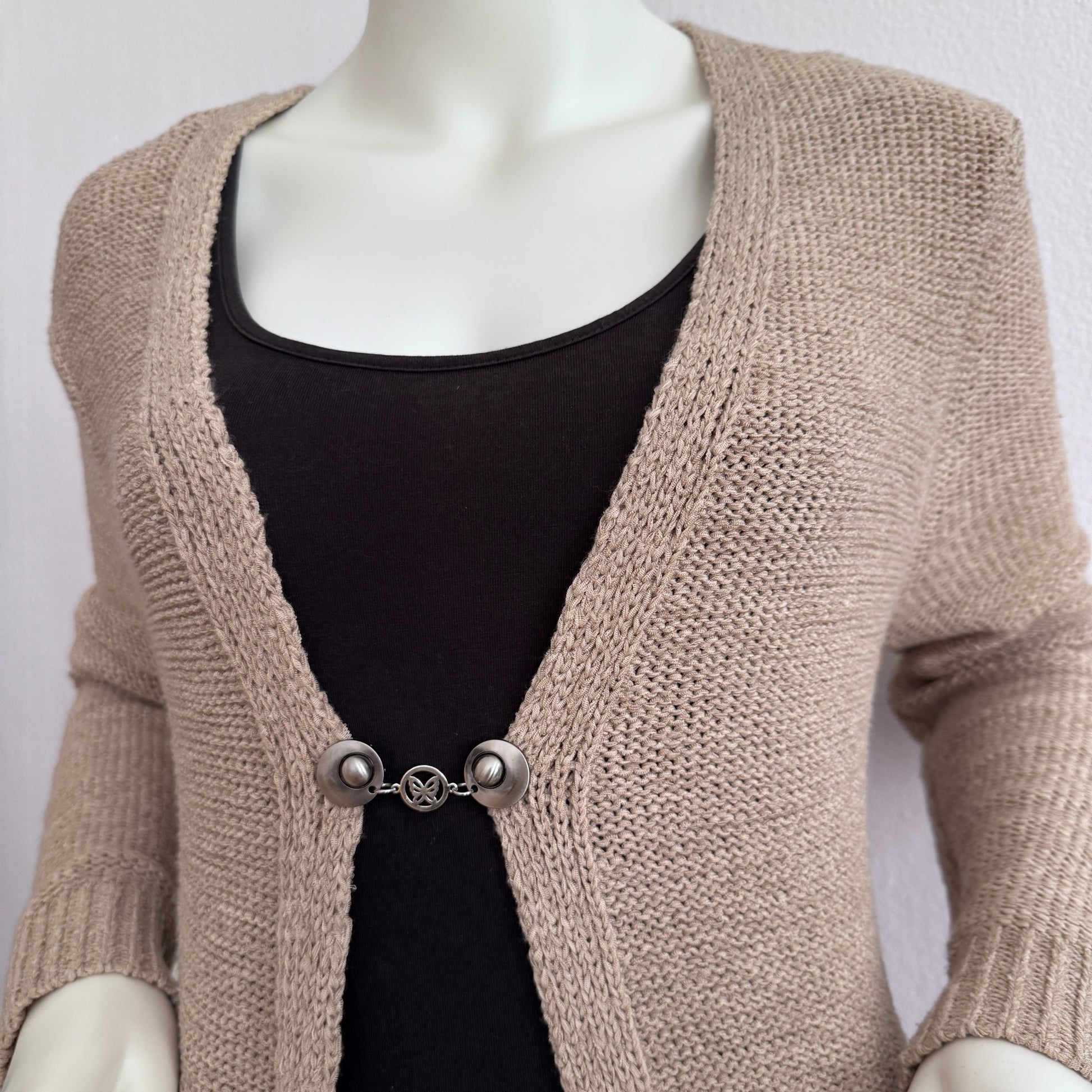 Vestsluiting De Geluksvlinder gedragen op een beige gebreid vest, elegante Fashionclip met zilverkleurige clips en vlindervormige tussenbedel.