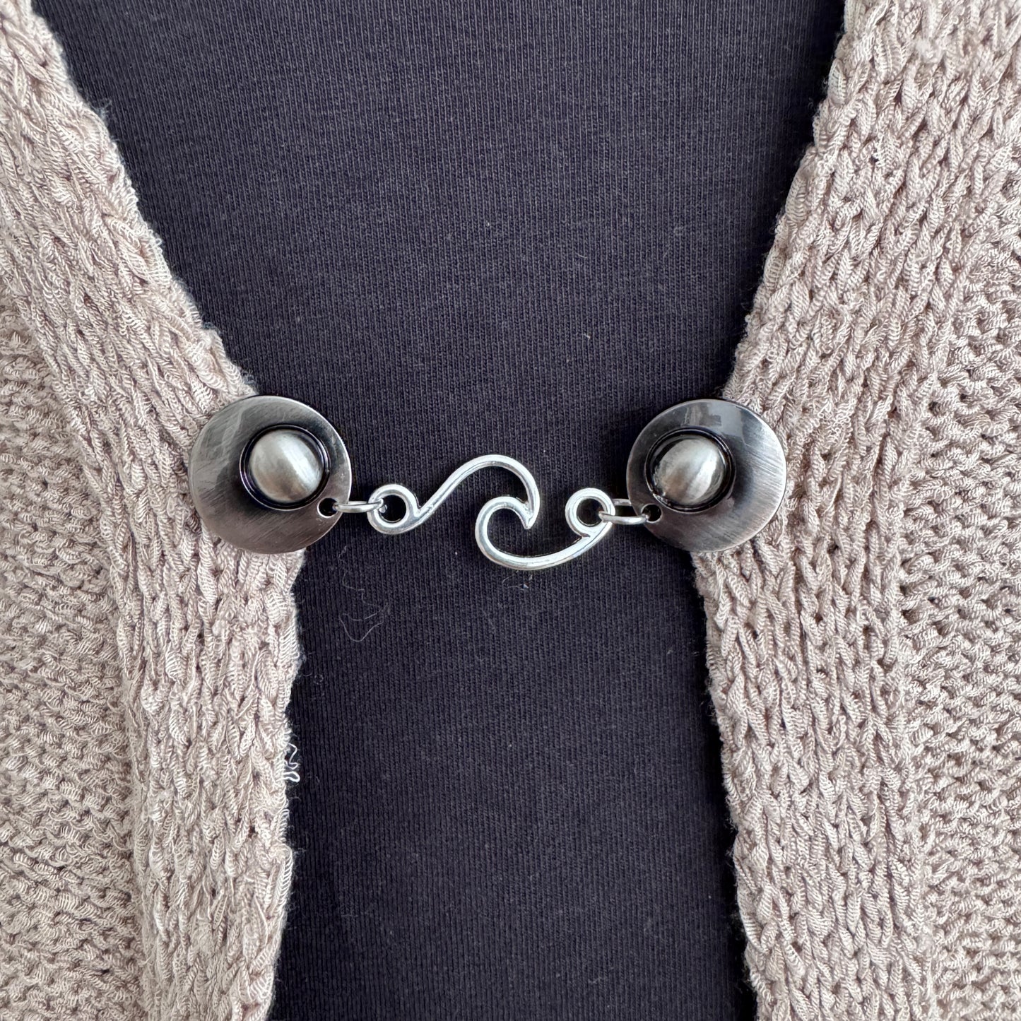 Vestsluiting De Golf in close-up op een gebreid vest, elegante Fashionclip met zilverkleurige clips en golvende tussenbedel.