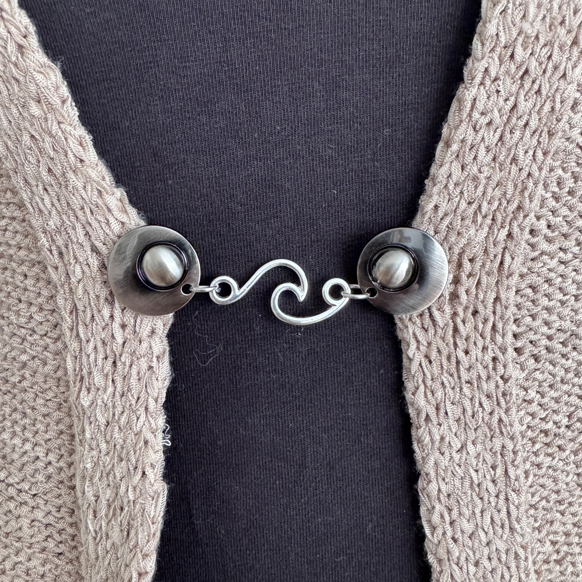 Vestsluiting De Golf in close-up op een gebreid vest, elegante Fashionclip met zilverkleurige clips en golvende tussenbedel.
