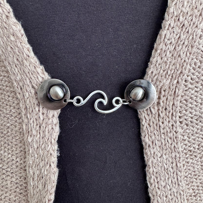 Vestsluiting De Golf in close-up op een gebreid vest, elegante Fashionclip met zilverkleurige clips en golvende tussenbedel.