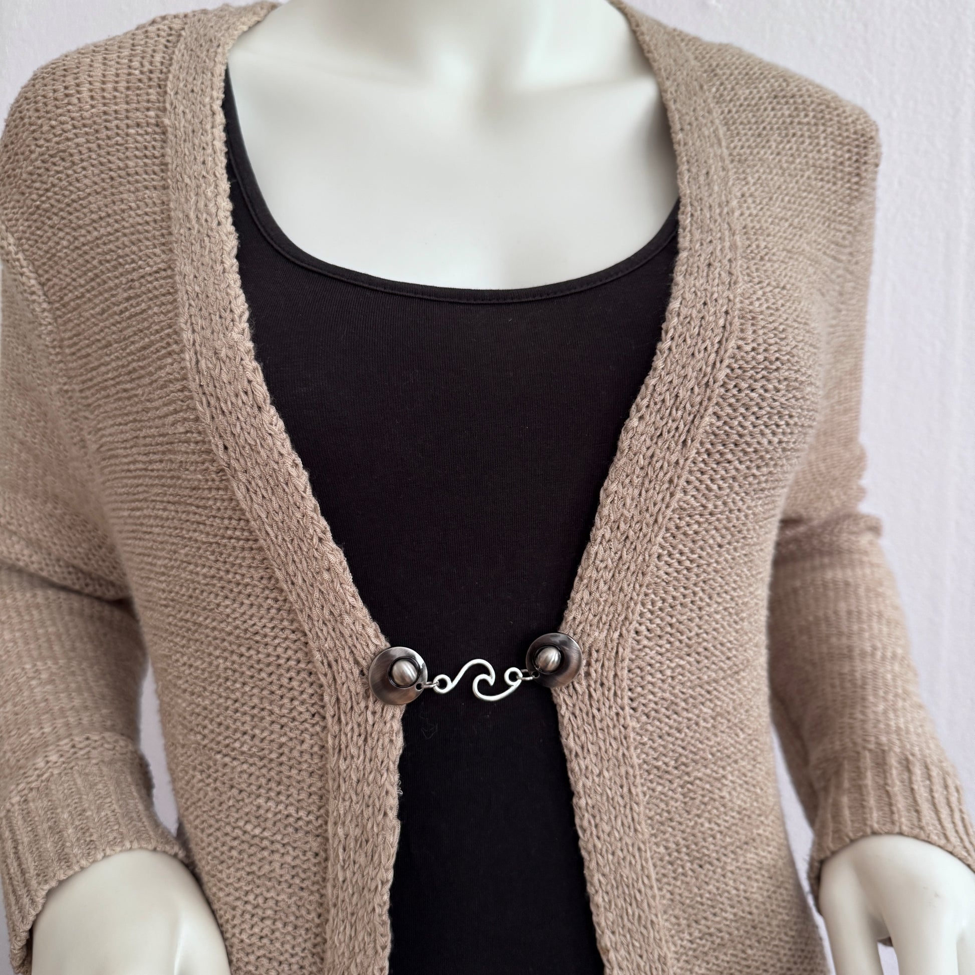 Vestsluiting De Golf gedragen op een beige gebreid vest, elegante Fashionclip met zilverkleurige clips en golvende tussenbedel.