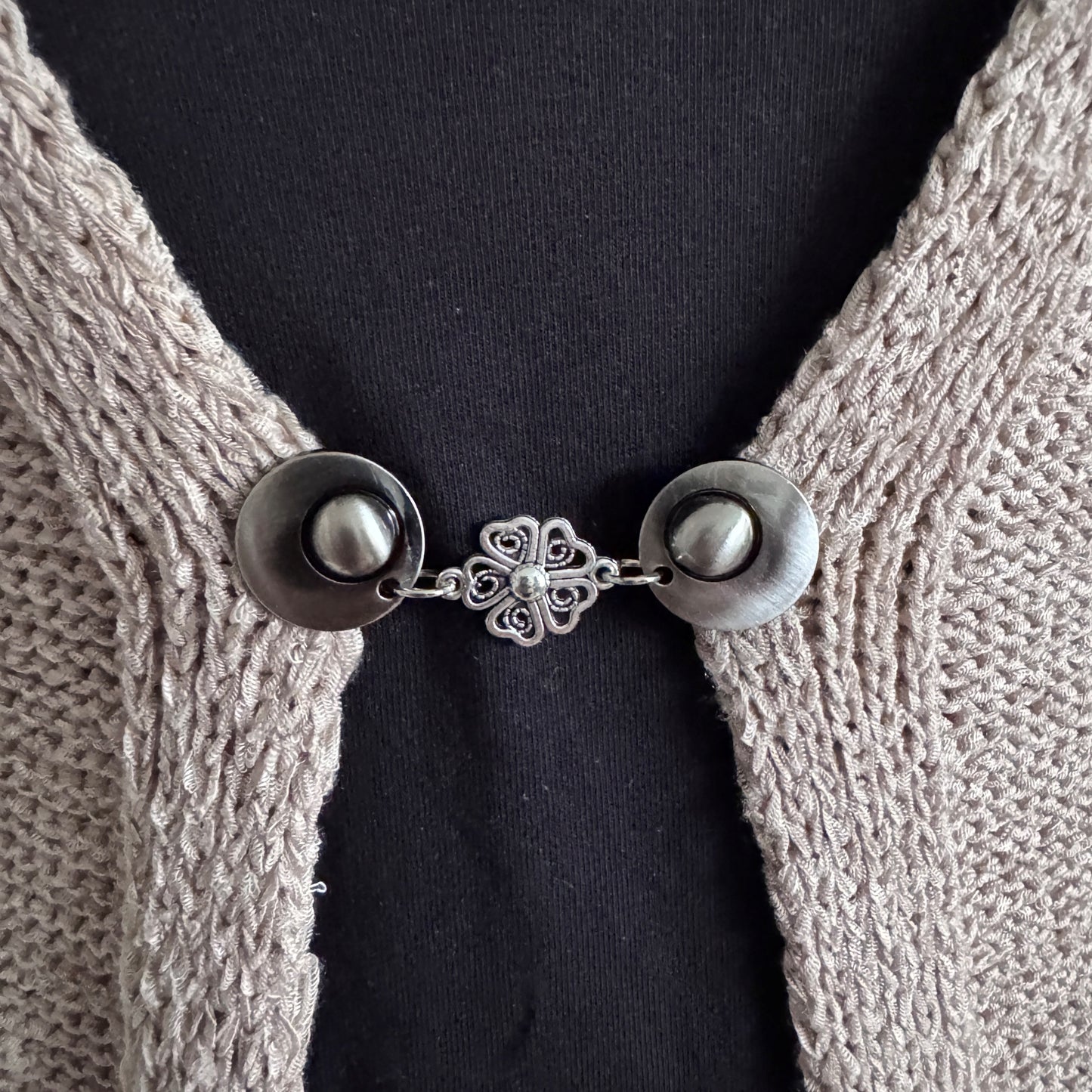 Vestsluiting De Hartenbloem in close-up op een gebreid vest, elegante Fashionclip met zilverkleurige clips en hartvormige bloem tussenbedel.