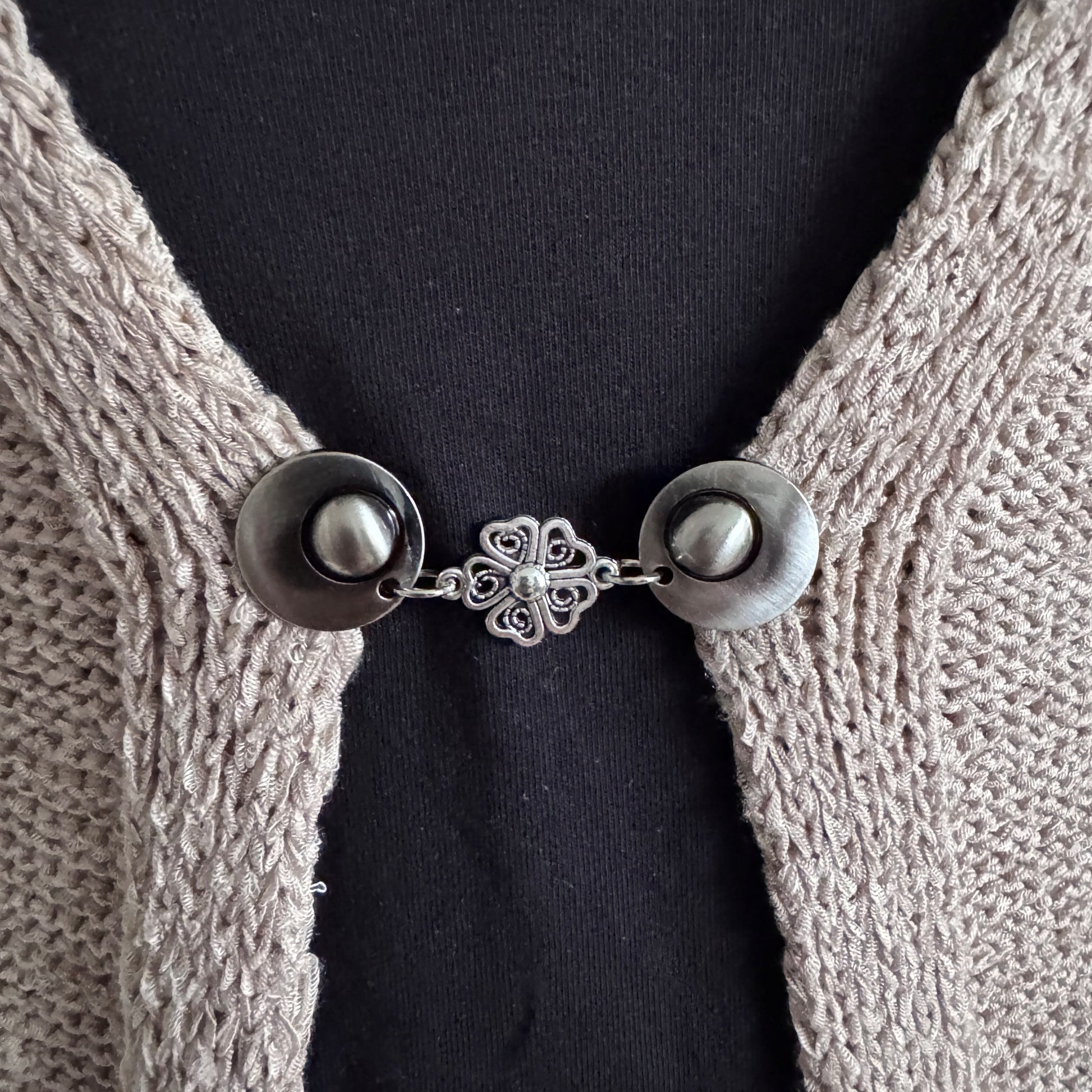 Vestsluiting De Hartenbloem in close-up op een gebreid vest, elegante Fashionclip met zilverkleurige clips en hartvormige bloem tussenbedel.