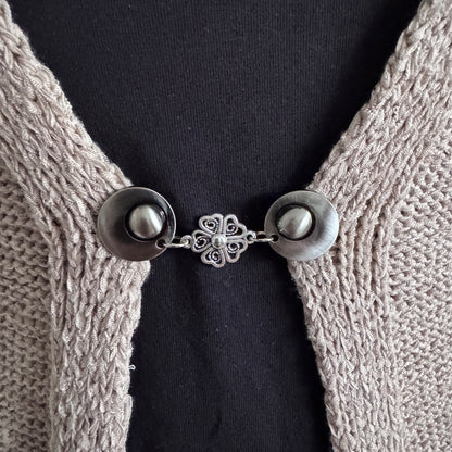 Vestsluiting De Hartenbloem in close-up op een gebreid vest, elegante Fashionclip met zilverkleurige clips en hartvormige bloem tussenbedel.