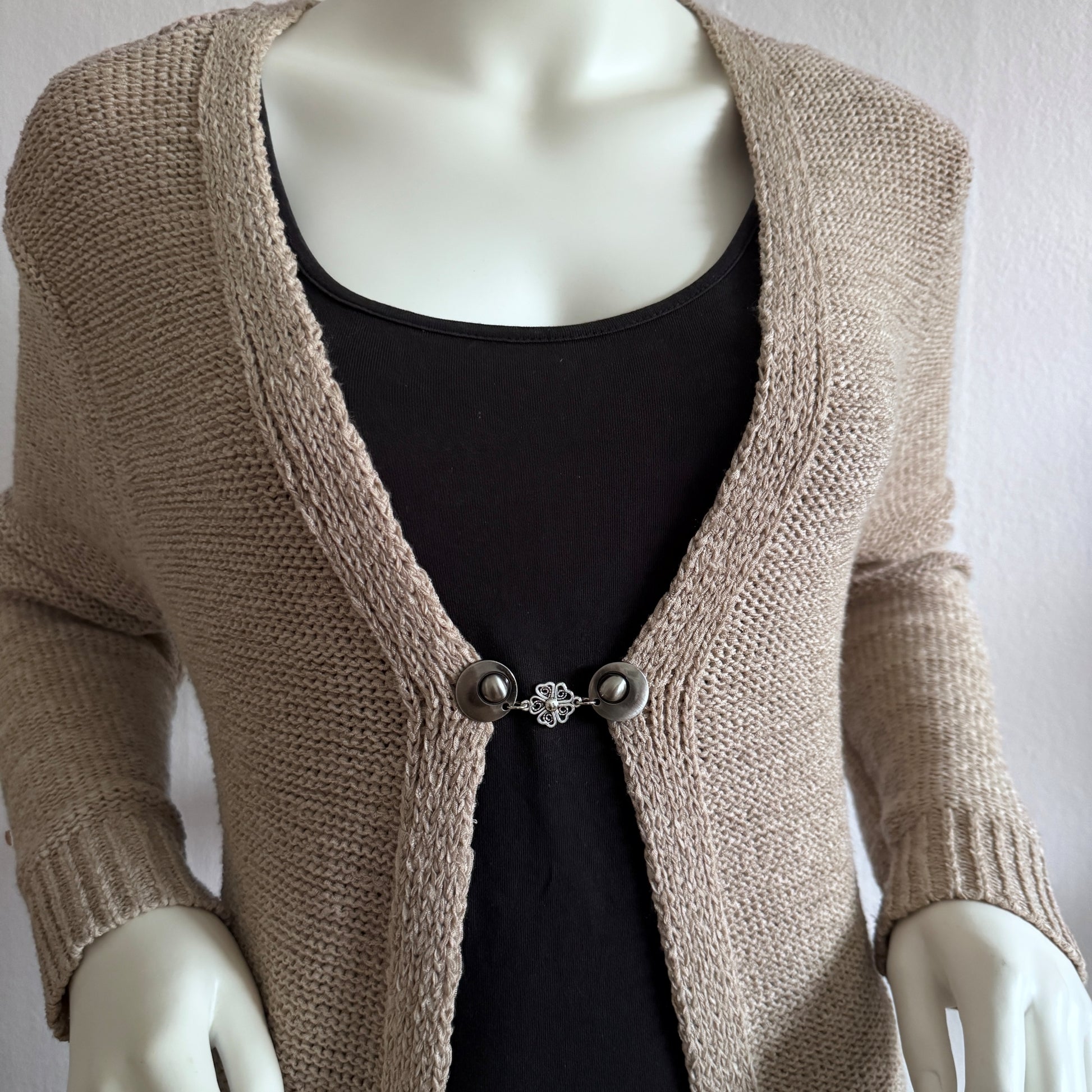 Vestsluiting De Hartenbloem gedragen op een beige gebreid vest, elegante Fashionclip met zilverkleurige clips en hartvormige bloem tussenbedel.